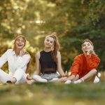 Three friends sitting on grass, enjoying a sunny outdoor day in the park.